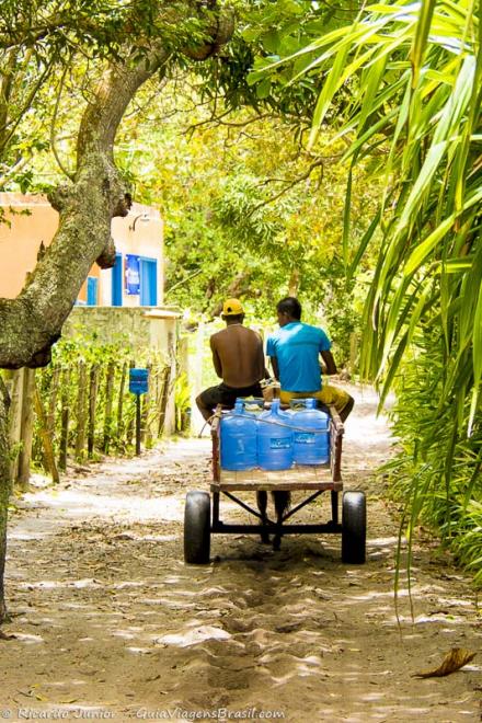 Imagem de dois entregadores de galões de água pelas ruas de areia em Caraiva.